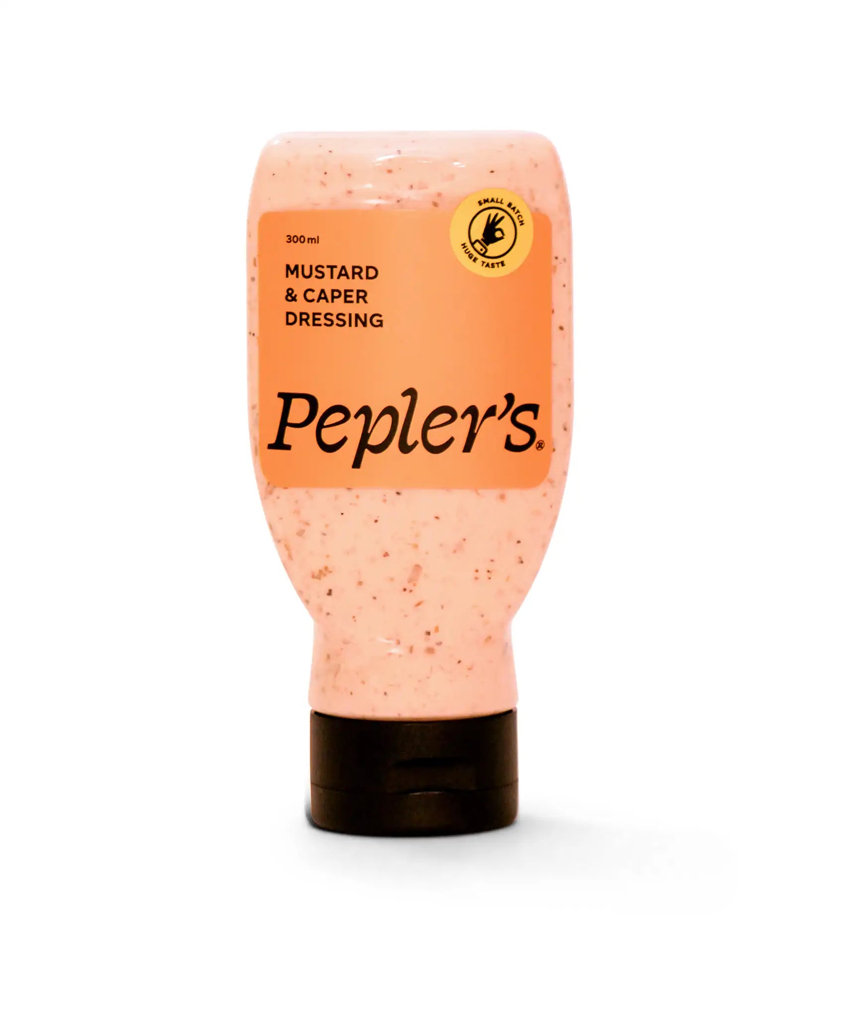A bottle of Pepler's mustard and caper dressing, featuring a soft pink colour with visible specks throughout. The front label is orange with black text that reads "300 ml Mustard & Capers Dressing," along with a small circular logo stating "Small Batch Huge Taste." The bottle has a black base and is positioned against a plain white background.